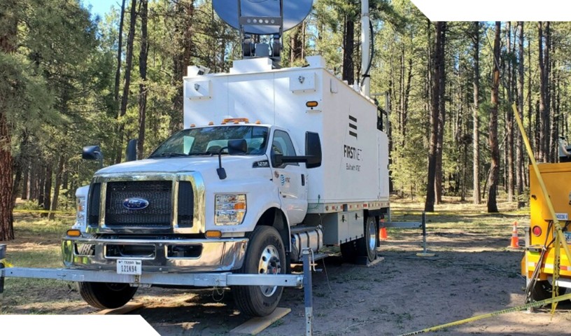 White FirstNet SatCOLT vehicle in the forest, connected to external power cart.