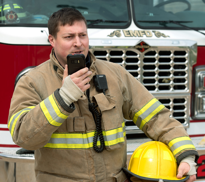Firefighter talking into mobile device in front of truck.