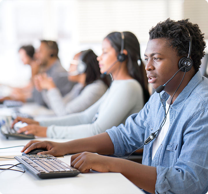 A group of call center employees seated in a row at desks, wearing headsets and working on desktop computers.
