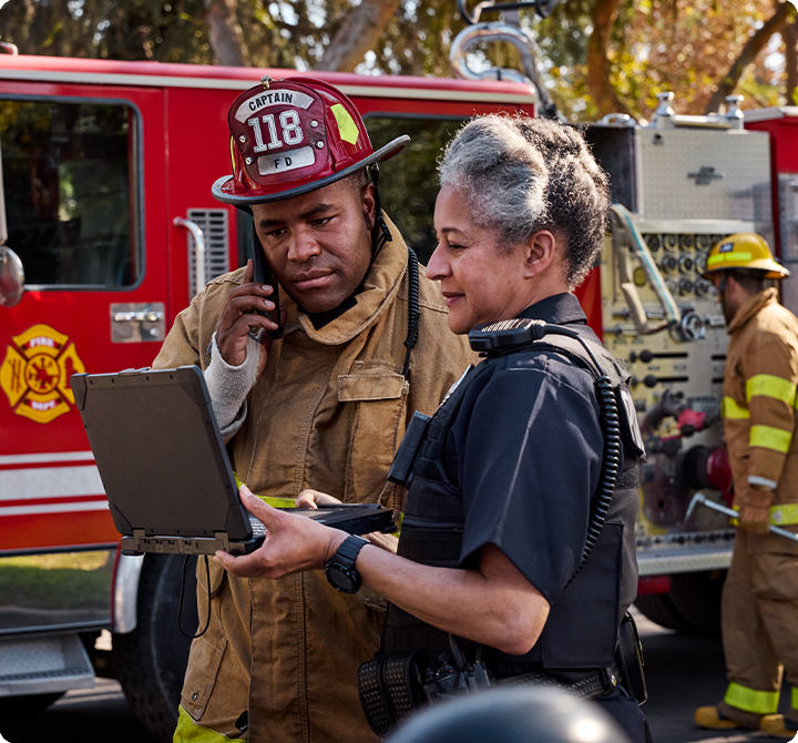 Firefighter using mobile and viewing laptop on the scene with police officer