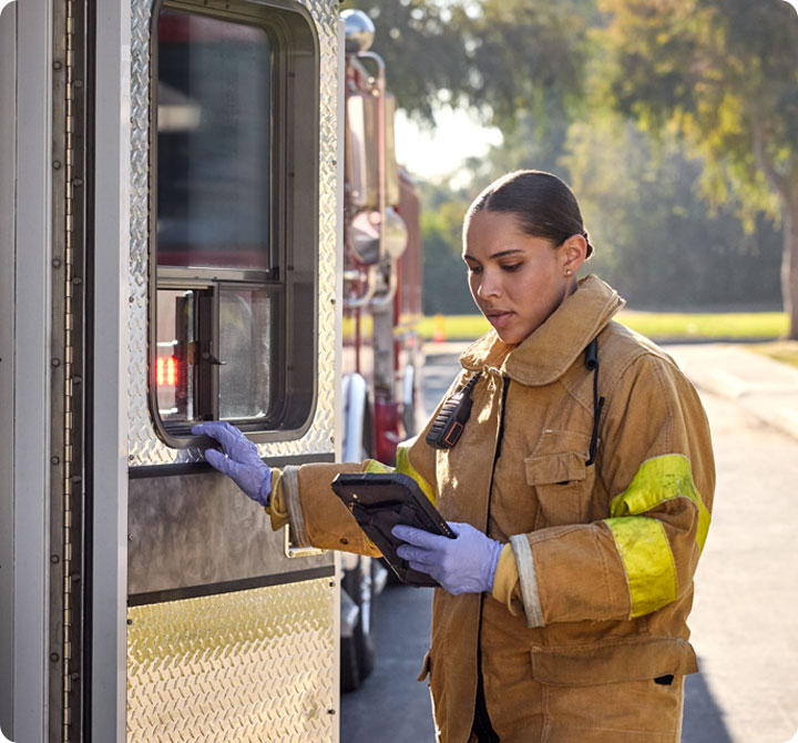 Female firefigher on FirstNet device standing near an ambulance 