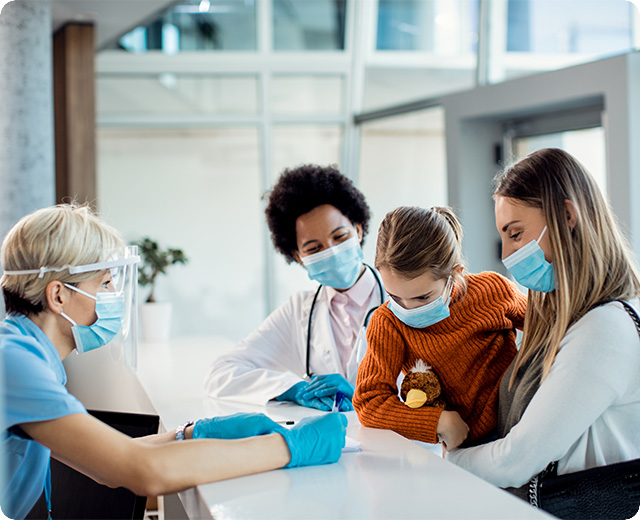 Mom holding child at hospital check-in with nurses surrounding them.