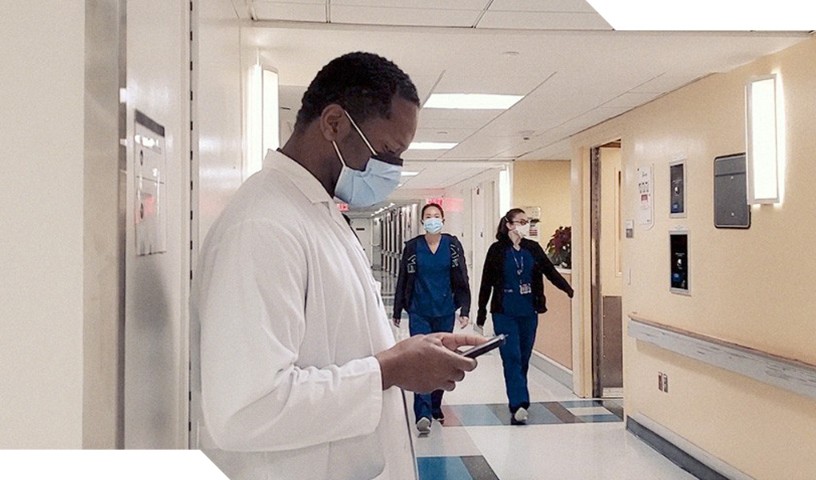 Masked doctor looking down at device in the hospital hallway, with 2 masked nurses approaching