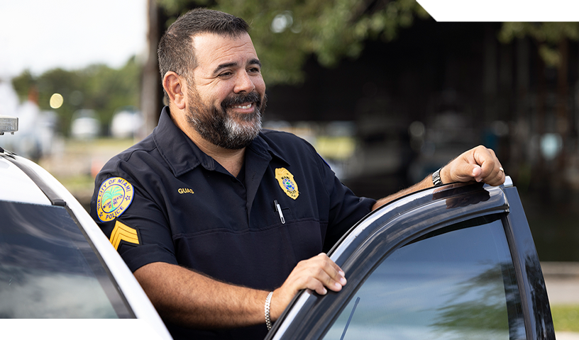 Police officer standing by police card door smiling