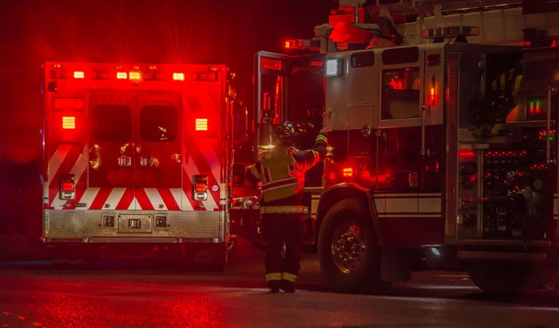 FirstNet responder fireman jumps back into his truck, at night, with bright red lights emitting from the EMT brake lights and reflecting the wet street