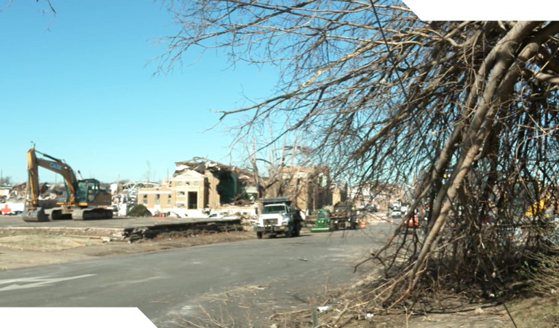 Clean up effort after Kentucky tornado in December 2021 (broken tree branches with power lines down and excavator in background cleaning up)